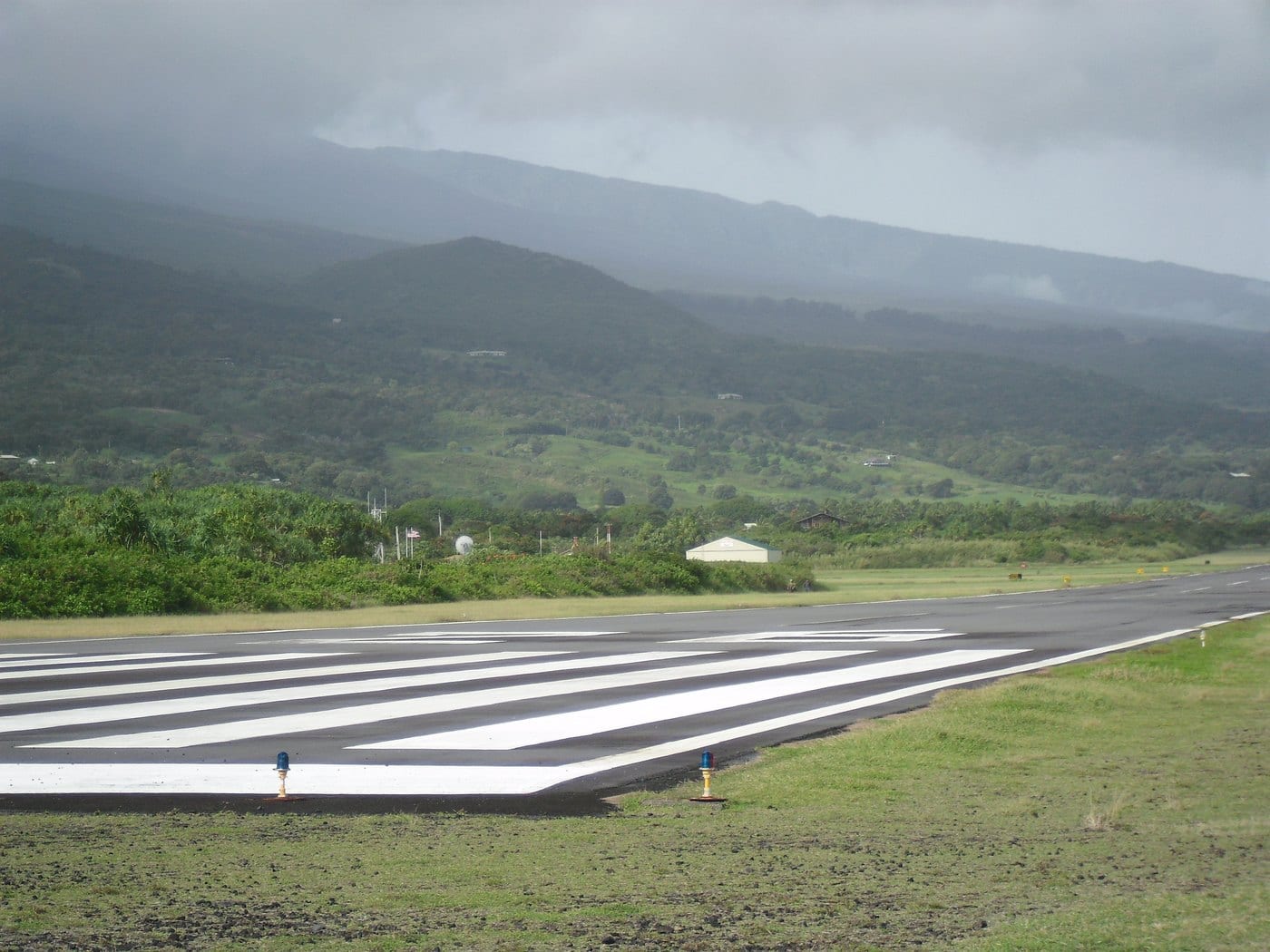 Runway 26 at Hāna Airport with green slopes and low clouds beyond