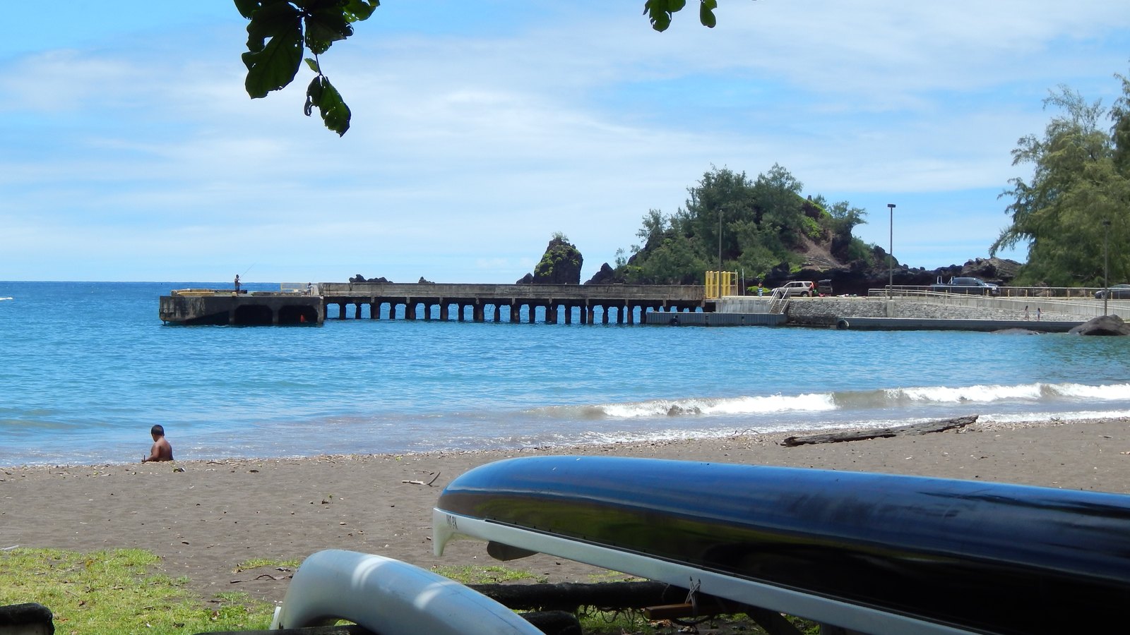Hāna Bay with the historic concrete wharf, shoreline launch area, and Puʻu Kaʻuiki beyond