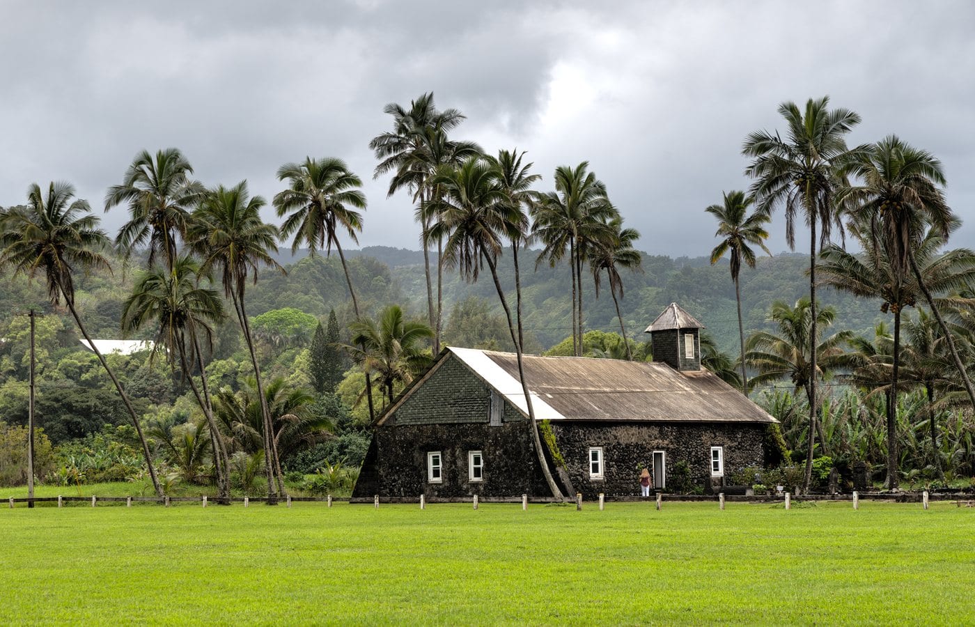 Stone walls and white gable of Keʻanae Congregational Church among palms and trees