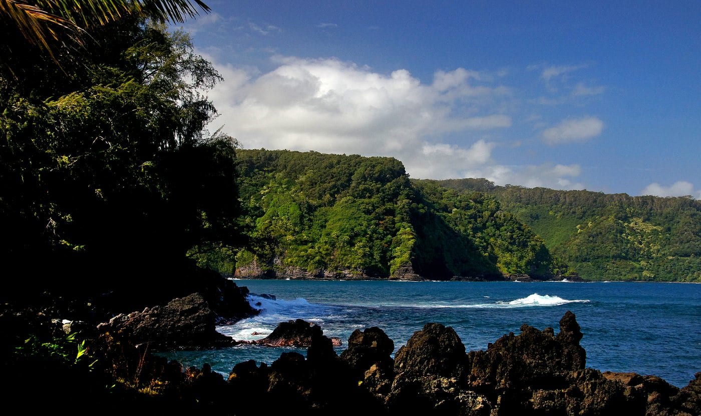 Dark lava rocks, breaking waves, and a green coastal slope at Keʻanae Peninsula