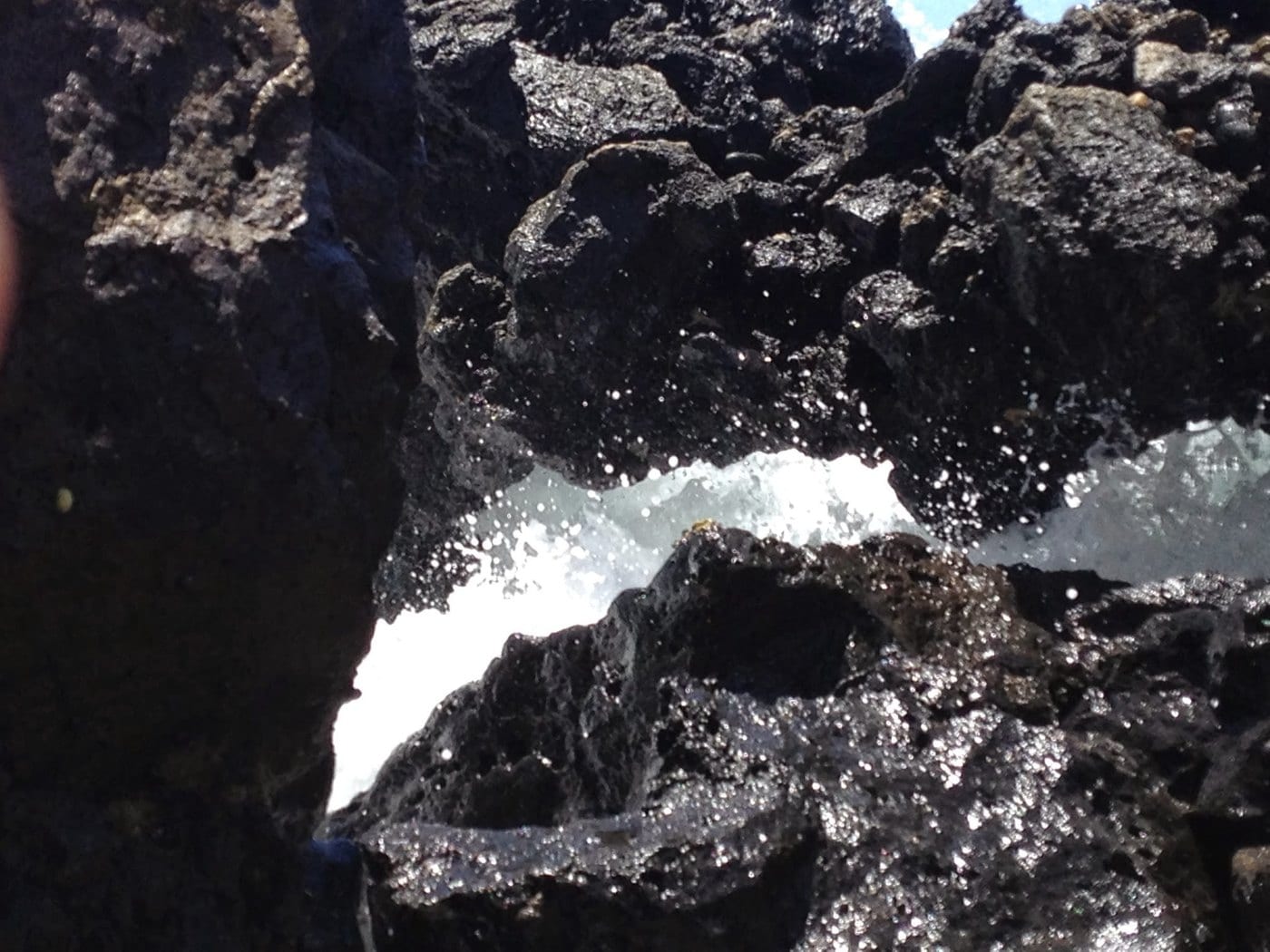 Rough black lava, sparse dryland vegetation, and surf at Keoneʻōʻio