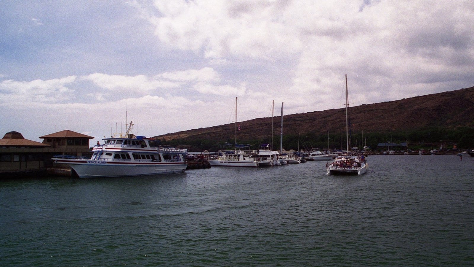 Tour boats and sailboats inside Māʻalaea Harbor beneath the dry hills above Māʻalaea