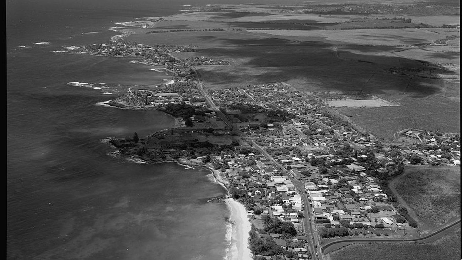 Aerial view along Pāʻia, its shoreline, Hāna Highway, and surrounding agricultural fields