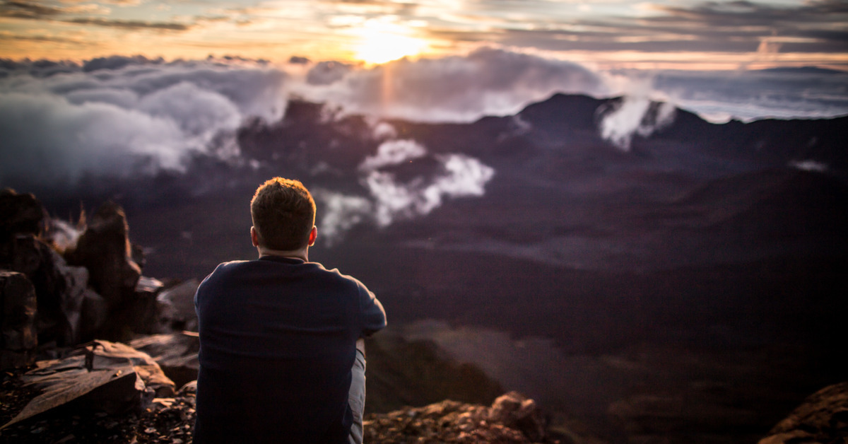 A person takes a photo of the sunset as they stand on the rocks of the summit of Haleakala National Park.